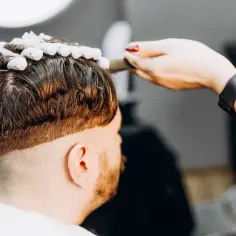 Fryzjerka zakłada wałki na włosy mężczyzny, przygotowując go do trwałej.